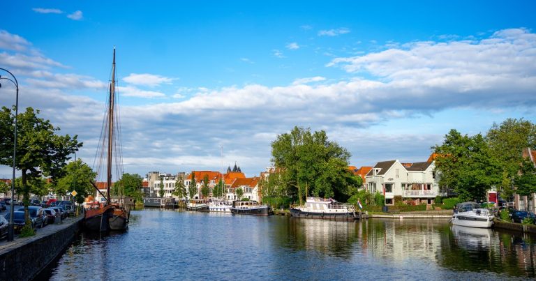 Een gracht in Haarlem met boten en historische panden onder een blauwe lucht