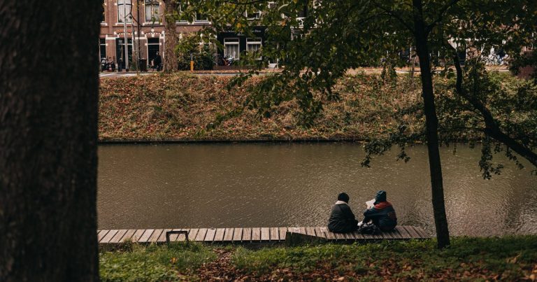 Een stel zit op een herfstdag aan de gracht, omringd door bomen