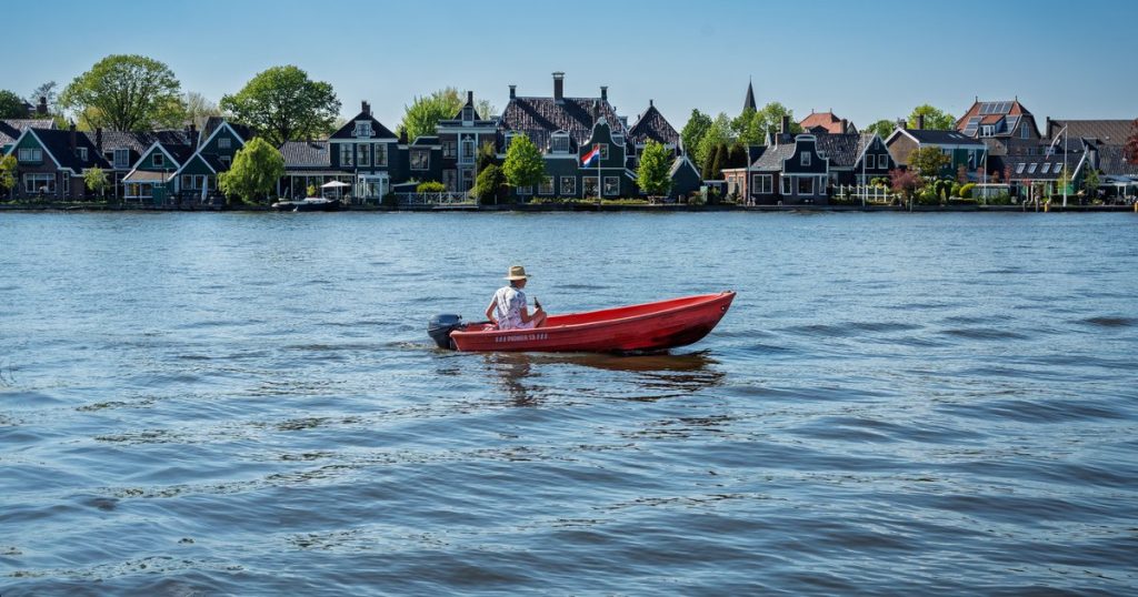 Iemand vaart in een rode boot langs de traditionele Zaanse huizen bij de Zaanse Schans