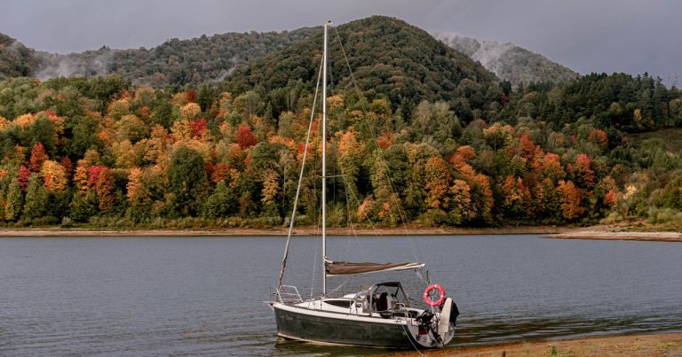 Een zeilboot op een meer met herfstkleuren aan de oever