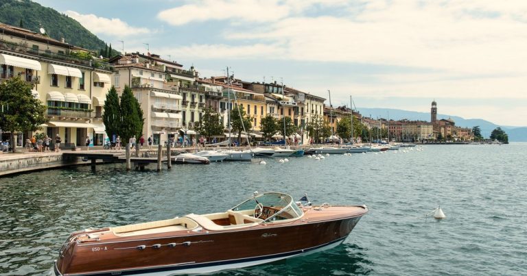 Luxe boot afgemeerd aan het Gardameer in Italië, met sfeervolle architectuur aan de oever.