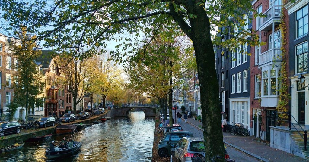Schilderachtig uitzicht op een Amsterdamse gracht in de herfst met boten, bomen en historische panden bij zonsondergang
