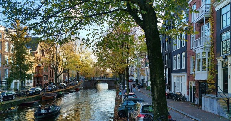 Schilderachtig uitzicht op een Amsterdamse gracht in de herfst met boten, bomen en historische panden bij zonsondergang