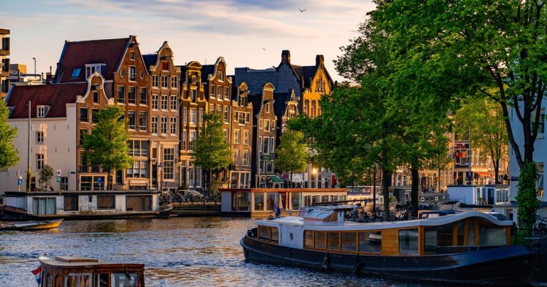 Amsterdamse grachtenpanden en boten bij zonsondergang met felgroene bomen