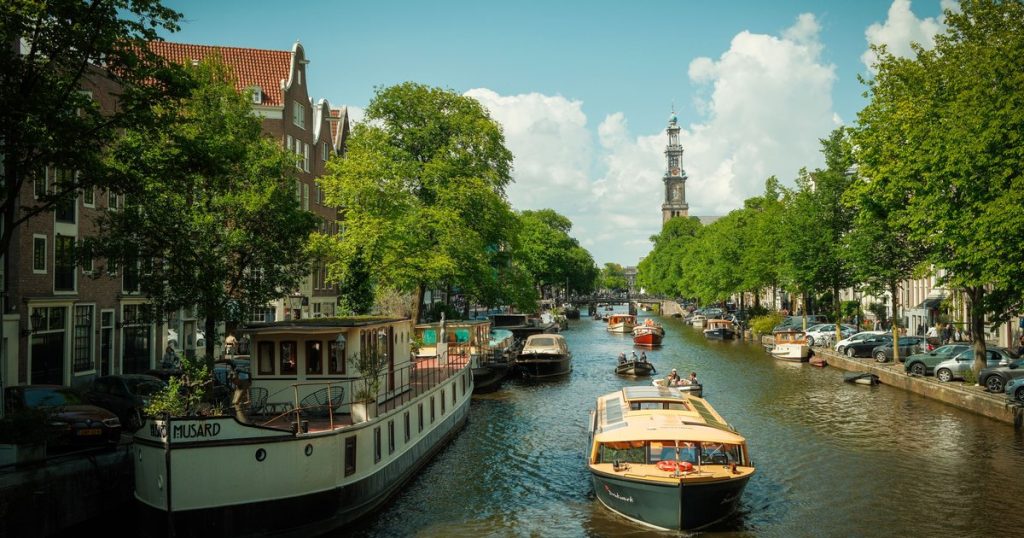 Amsterdamse gracht met historische boten en veel groen onder een strakblauwe hemel