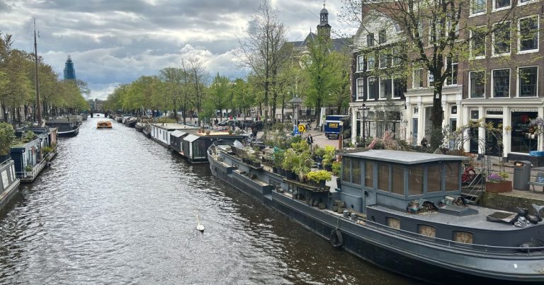 Uitzicht op een Amsterdamse gracht met woonboten en traditionele architectuur onder een bewolkte hemel