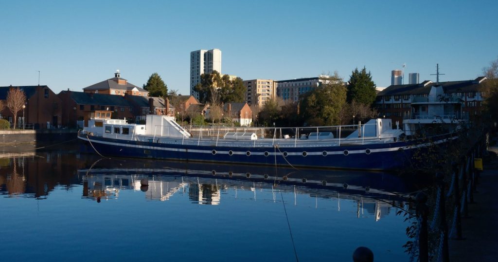 Een blauwe boot afgemeerd aan de kade langs de bebouwing van een rivier, onder een strakke lucht