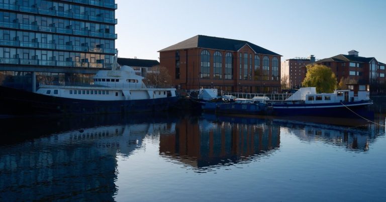 Boten afgemeerd langs moderne en klassieke gebouwen, weerspiegeld in rustig water