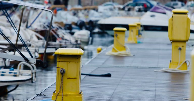 Gele bolders op een kade van een jachthaven, met boten erachter