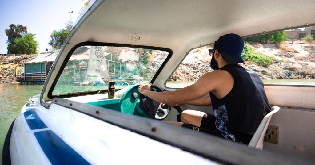 Man stuurt een motorboot langs een rustige oever in de zon