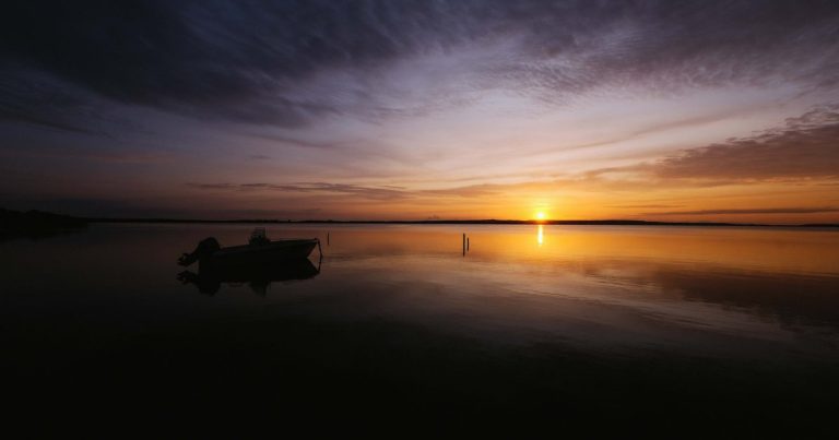 Zonsondergang boven een stil meer met het silhouet van een boot in het gouden licht