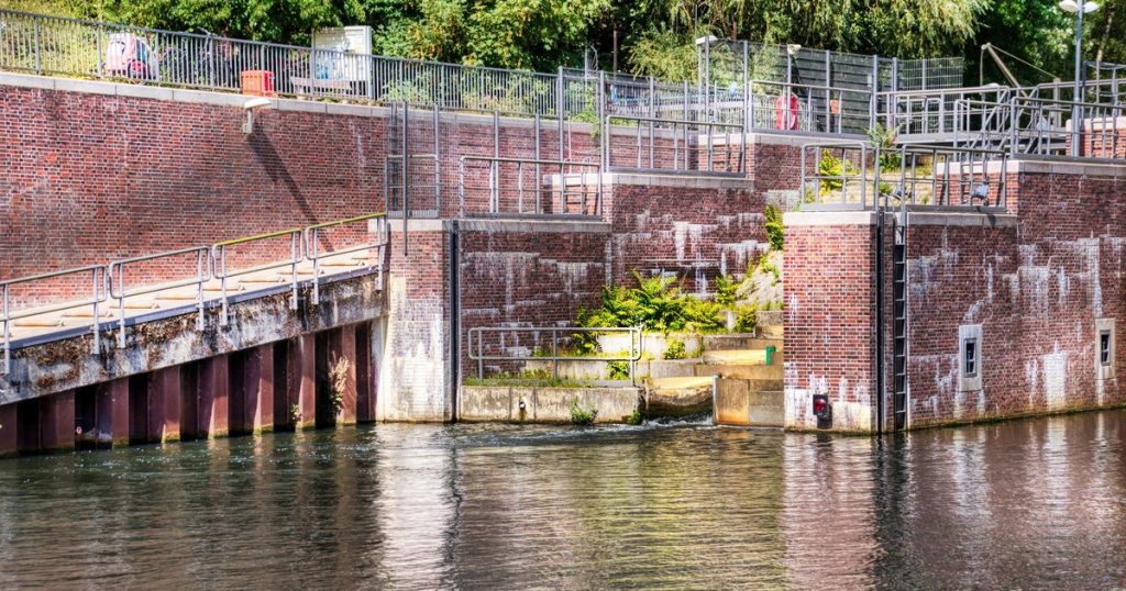 Een gemetselde sluis aan het water, met groen en leuningen langs de kant