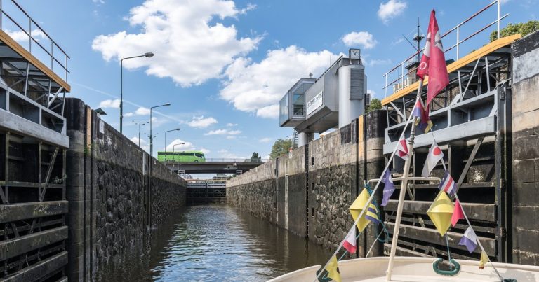Een boot vaart door een sluiskolk tussen hoge sluismuren