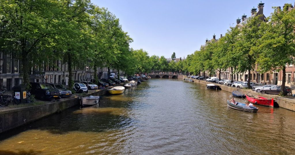 Een rustige Amsterdamse gracht met boten en historische gevels onder een strakke lucht