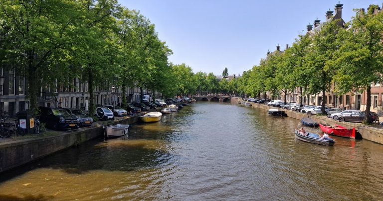 Een rustige Amsterdamse gracht met boten en historische gevels onder een strakke lucht