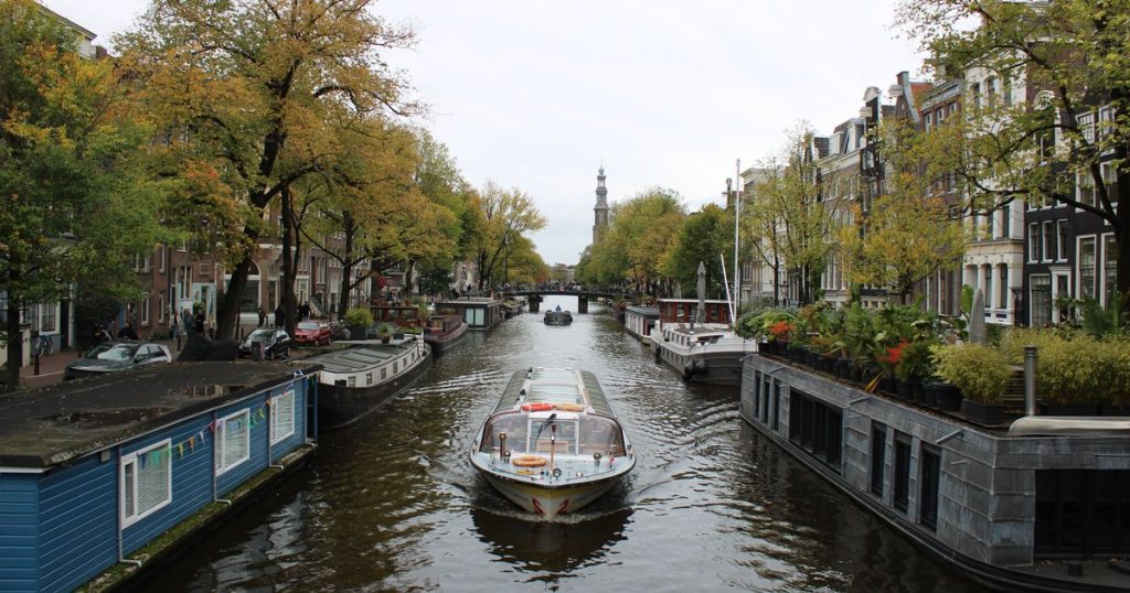 Een gracht met herfstbomen en woonboten langs het water