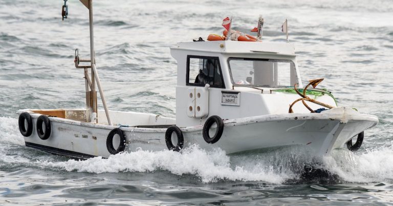 Een kleine witte vissersboot vaart op een bewolkte dag door woelig water
