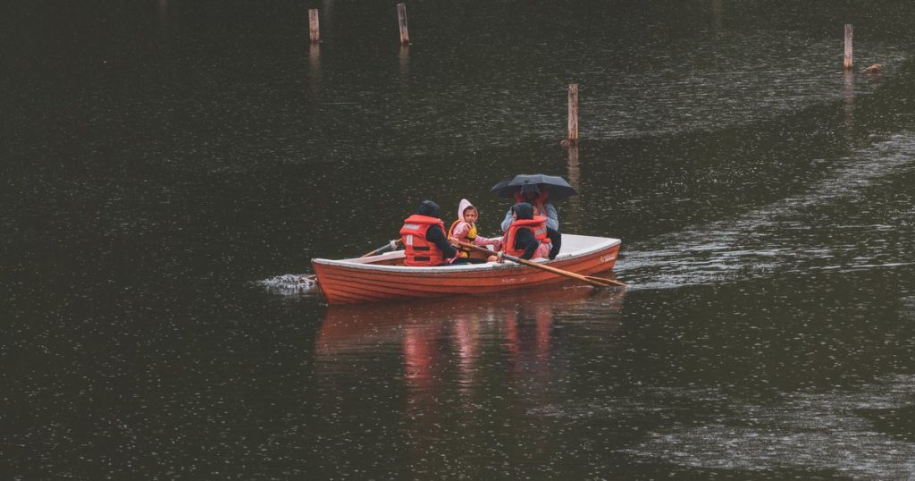 Mensen met reddingsvesten in een roeiboot op een meer in de regen
