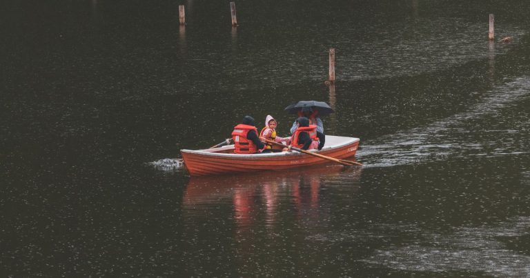 Mensen met reddingsvesten in een roeiboot op een meer in de regen