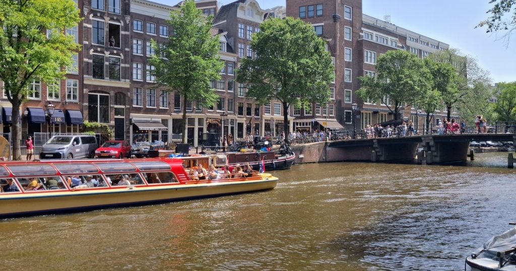 Een drukke Amsterdamse gracht met rondvaartboten onder een zonnige lucht