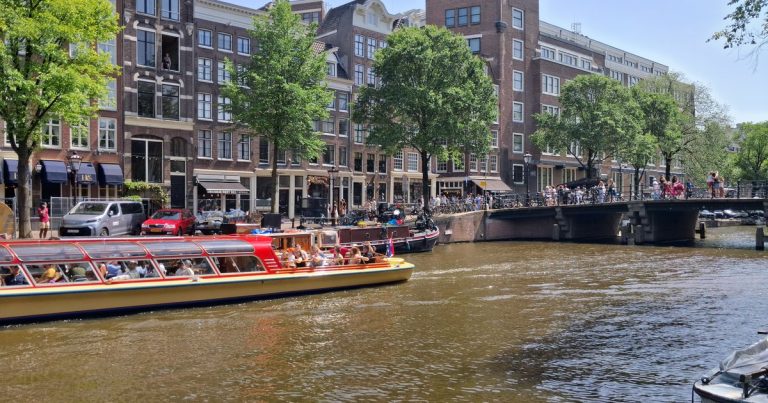Een drukke Amsterdamse gracht met rondvaartboten onder een zonnige lucht