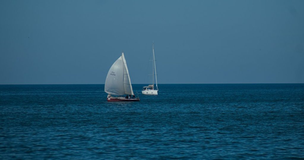 Twee zeilboten varen over een kalme blauwe zee onder een heldere hemel