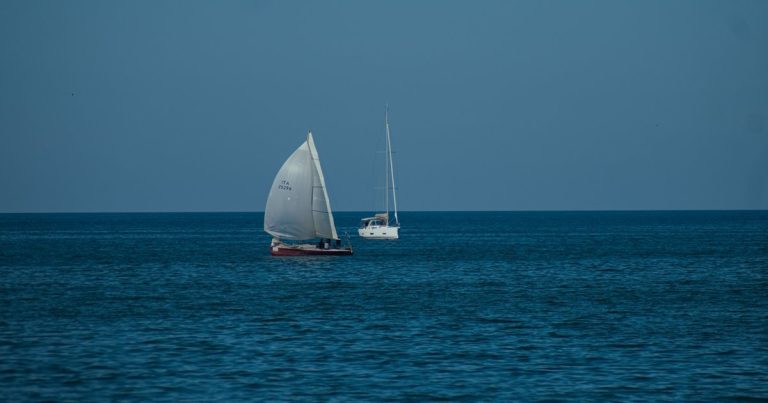 Twee zeilboten varen over een kalme blauwe zee onder een heldere hemel