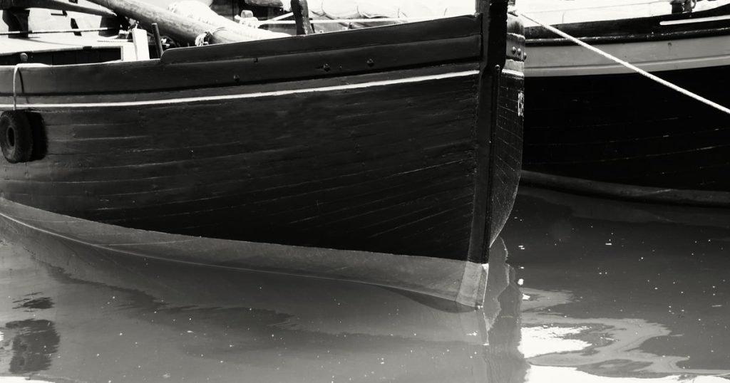 Zwart-witfoto van vintage boten die weerspiegelen in het kalme water van een haven.