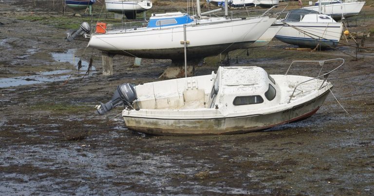 Meerdere boten liggen op een modderige oever, drooggevallen bij laag water.