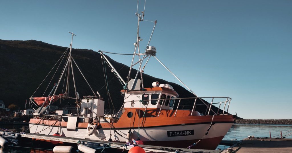Een aangemeerde vissersboot in de haven van Skarsvåg, Noorwegen, onder een heldere blauwe lucht.