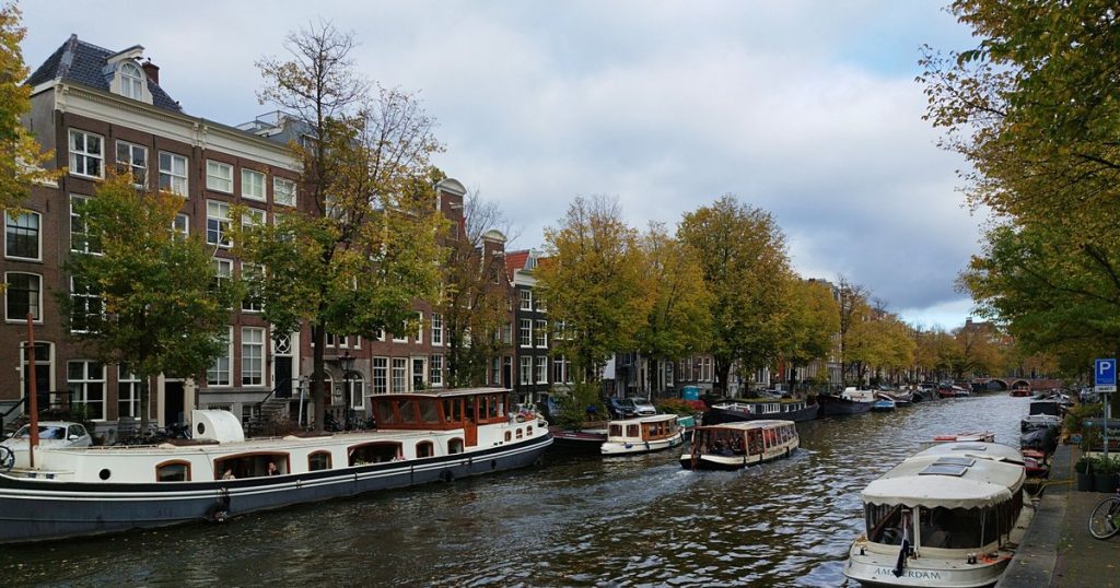Amsterdamse gracht in de herfst met boten en historische gebouwen langs kleurrijke bomen