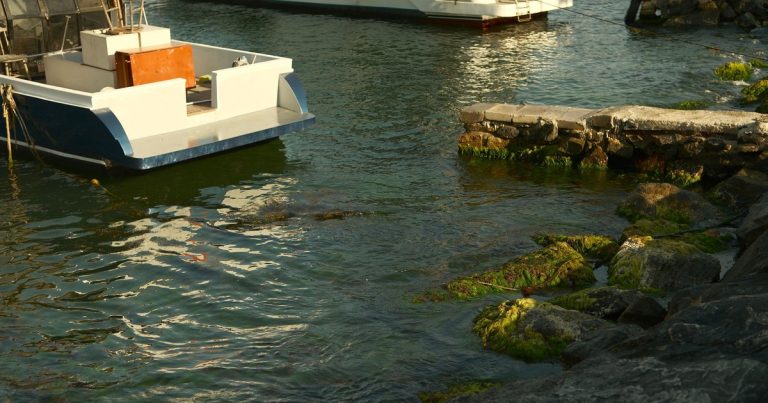 Twee boten afgemeerd in een rotsachtige haven met rotsen vol groene algen.