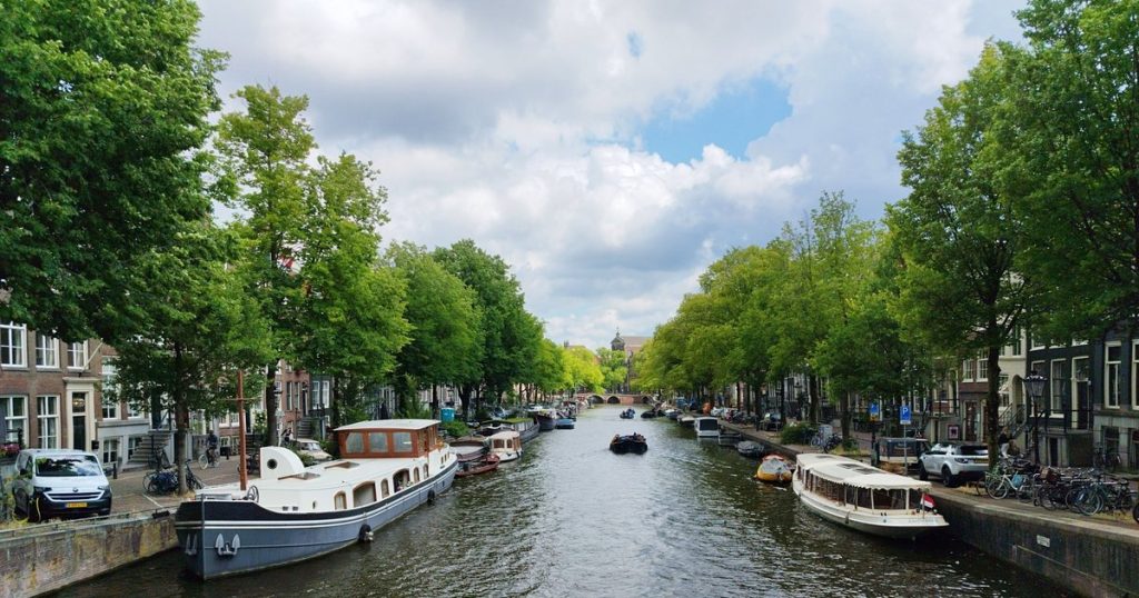 Schilderachtig uitzicht op een Amsterdamse gracht met boten en weelderige bomen onder een bewolkte lucht