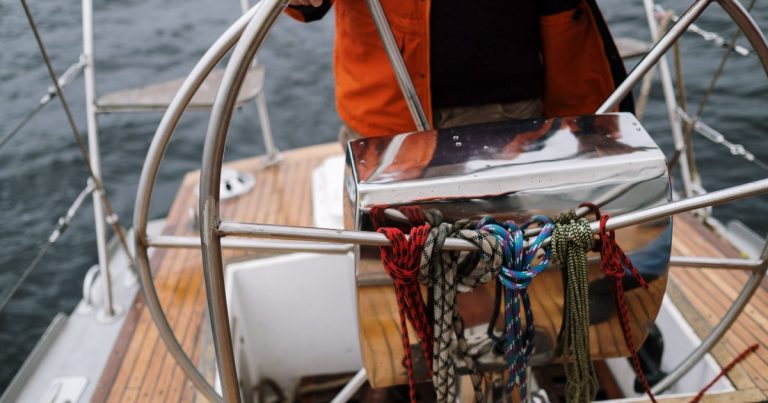 Close-up van een zeiler die het roer van een zeilboot vasthoudt en over open zee vaart