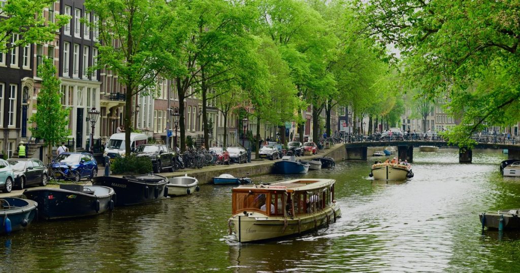 Amsterdamse gracht met boten, historische panden en groene bomen