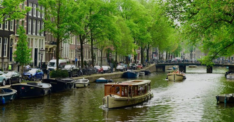 Amsterdamse gracht met boten, historische panden en groene bomen