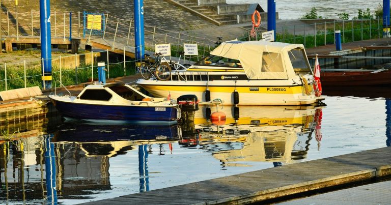 Twee aangemeerde boten in een jachthaven, weerspiegeld in het kalme rivierwater bij helder daglicht.
