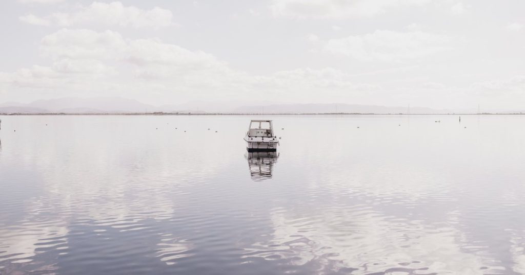 Boot drijft op kalm water in Sardinië, Italië, waarin de rustige lucht weerspiegelt