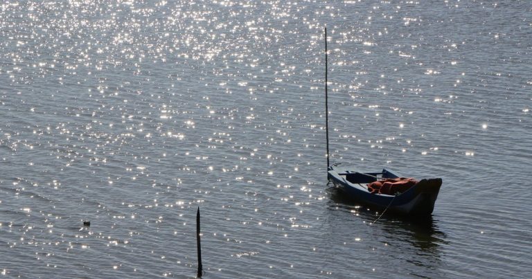 Een boot voor anker op het water met fonkelende zonlichtreflecties