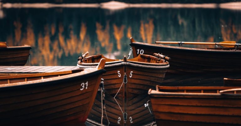 Houten boten afgemeerd op een meer waarin herfstbladeren weerspiegelen