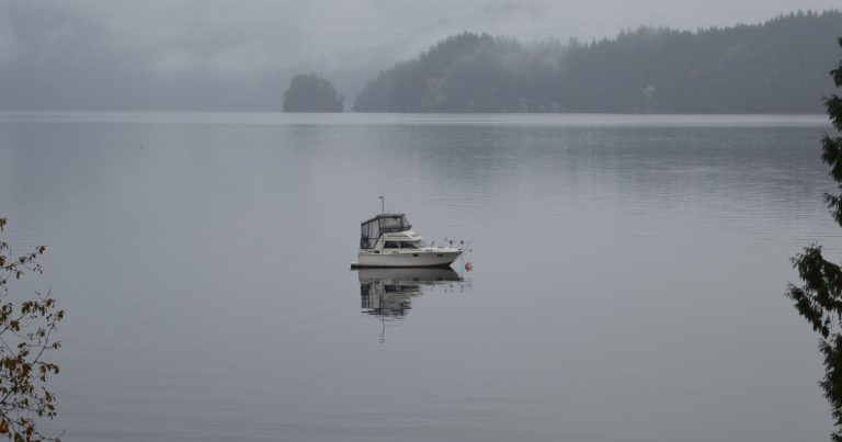 Eenzame boot drijft op een mistig meer in Brits-Columbia, omringd door kalm water en mist