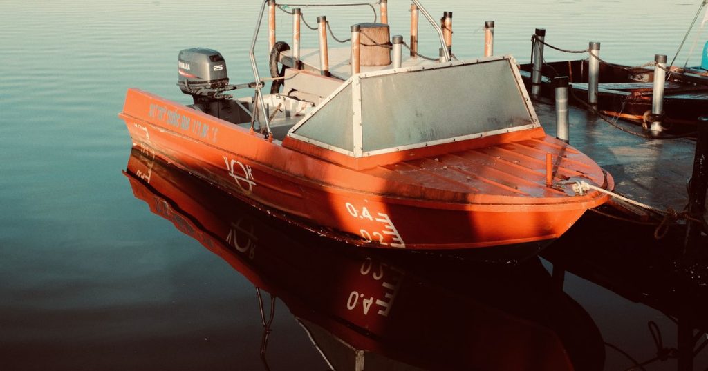 Rode motorboot aangemeerd aan een steiger, met weerspiegelingen in het kalme water.