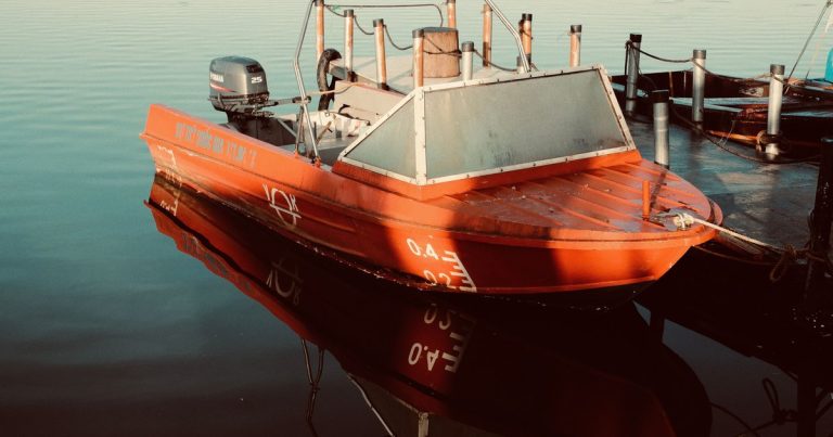 Rode motorboot aangemeerd aan een steiger, met weerspiegelingen in het kalme water.